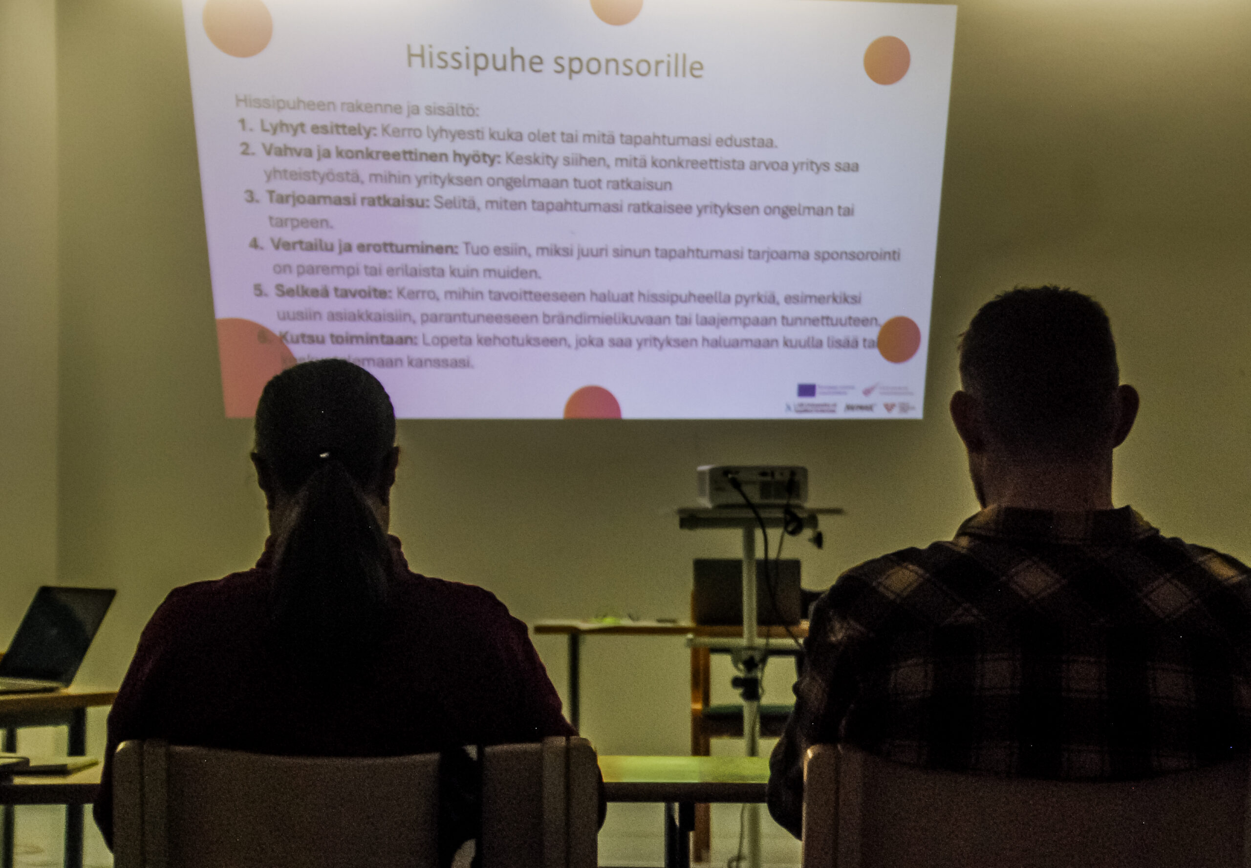 yleisö, taustalla kuva jossa tehtävänkuvaus hissipuheen muodostamiseksi