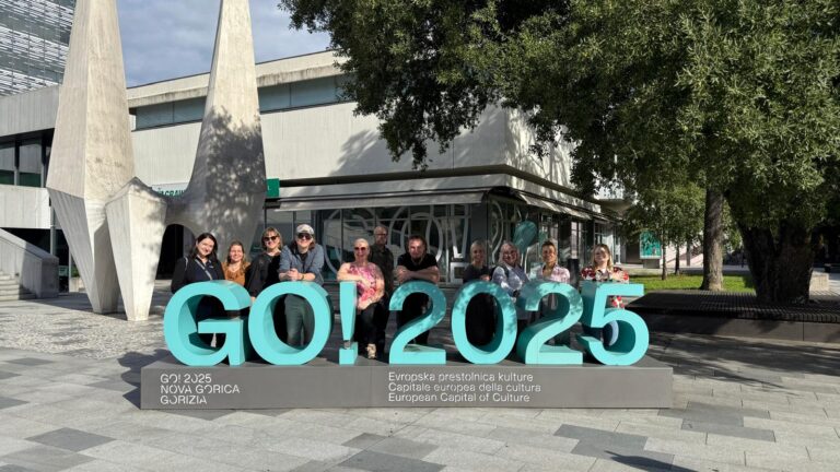 Ihmisiä ryhmäkuvassa ison GO! 2025 kyltin takana.